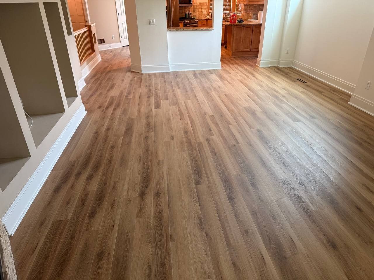 Luxury vinyl plank flooring in medium tan and brown tones installed in an open living area with white trim.