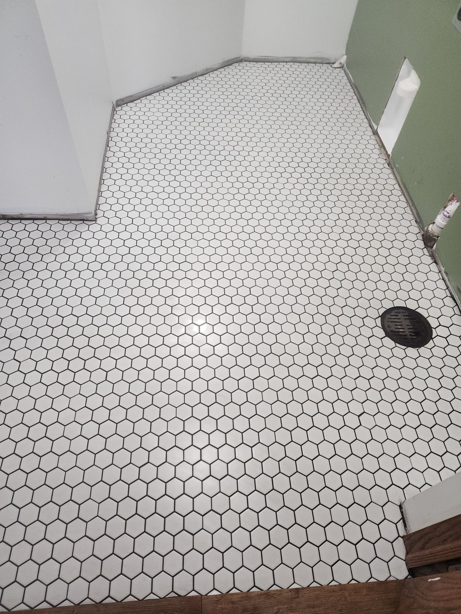 Small white hexagonal mosaic tiles installed on a bathroom floor with gray grout lines and a central drain.
