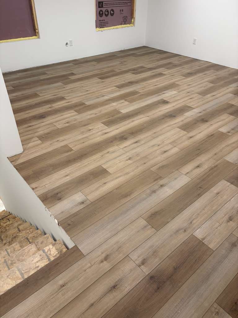 Newly installed light brown plank LVP flooring in an empty basement room with white walls.