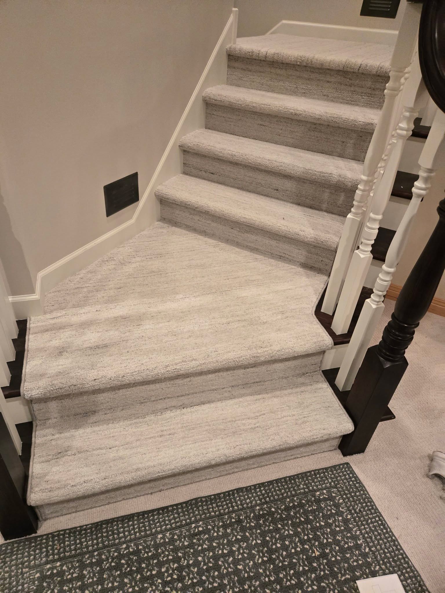 Carpeted staircase with gray treads and white landing, white railings, and dark stair nosing.