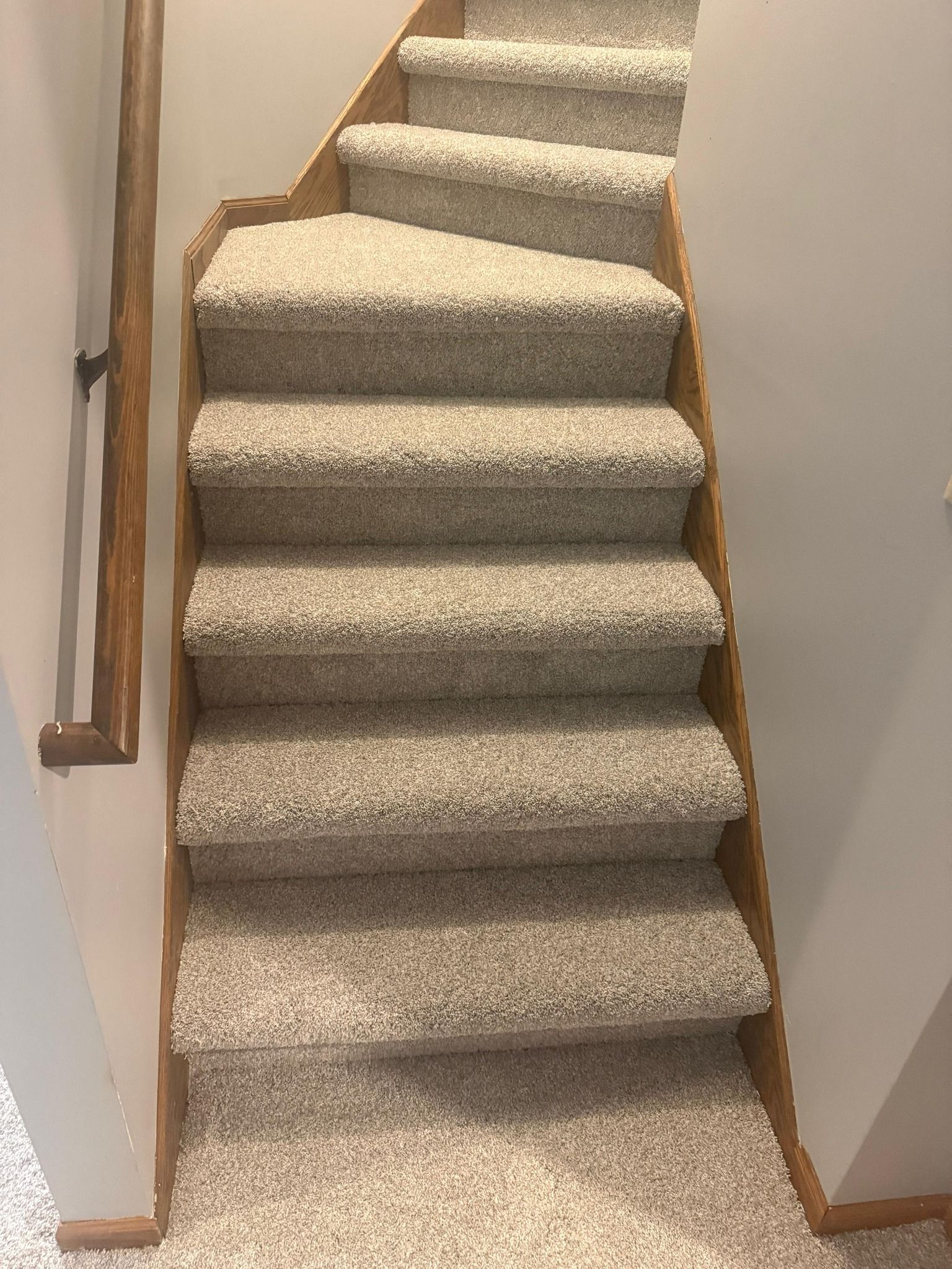 Staircase with beige carpet and wood trim installed in a residential home.