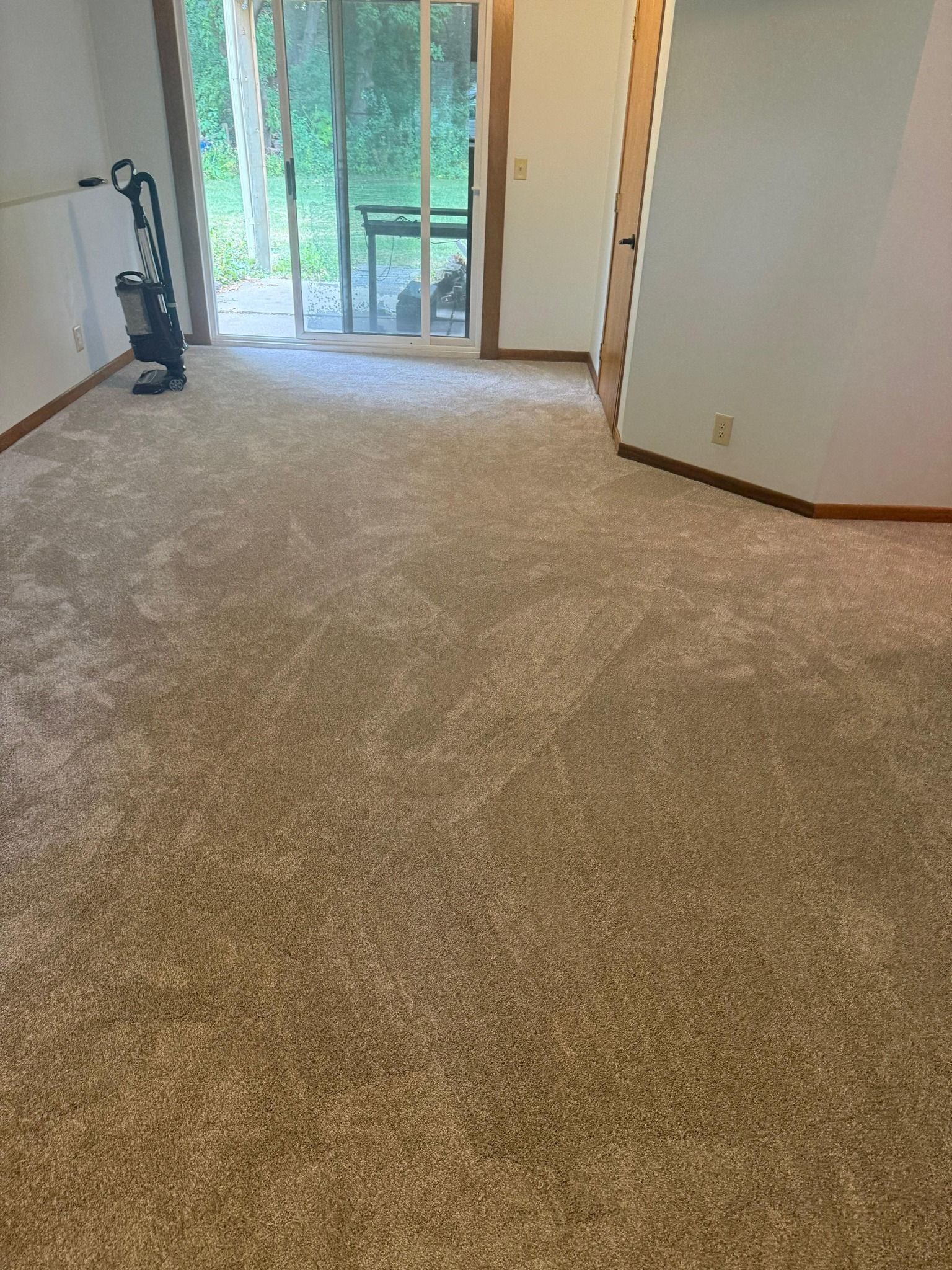 Newly installed tan carpet in a living room with patio doors and brown wood trim.