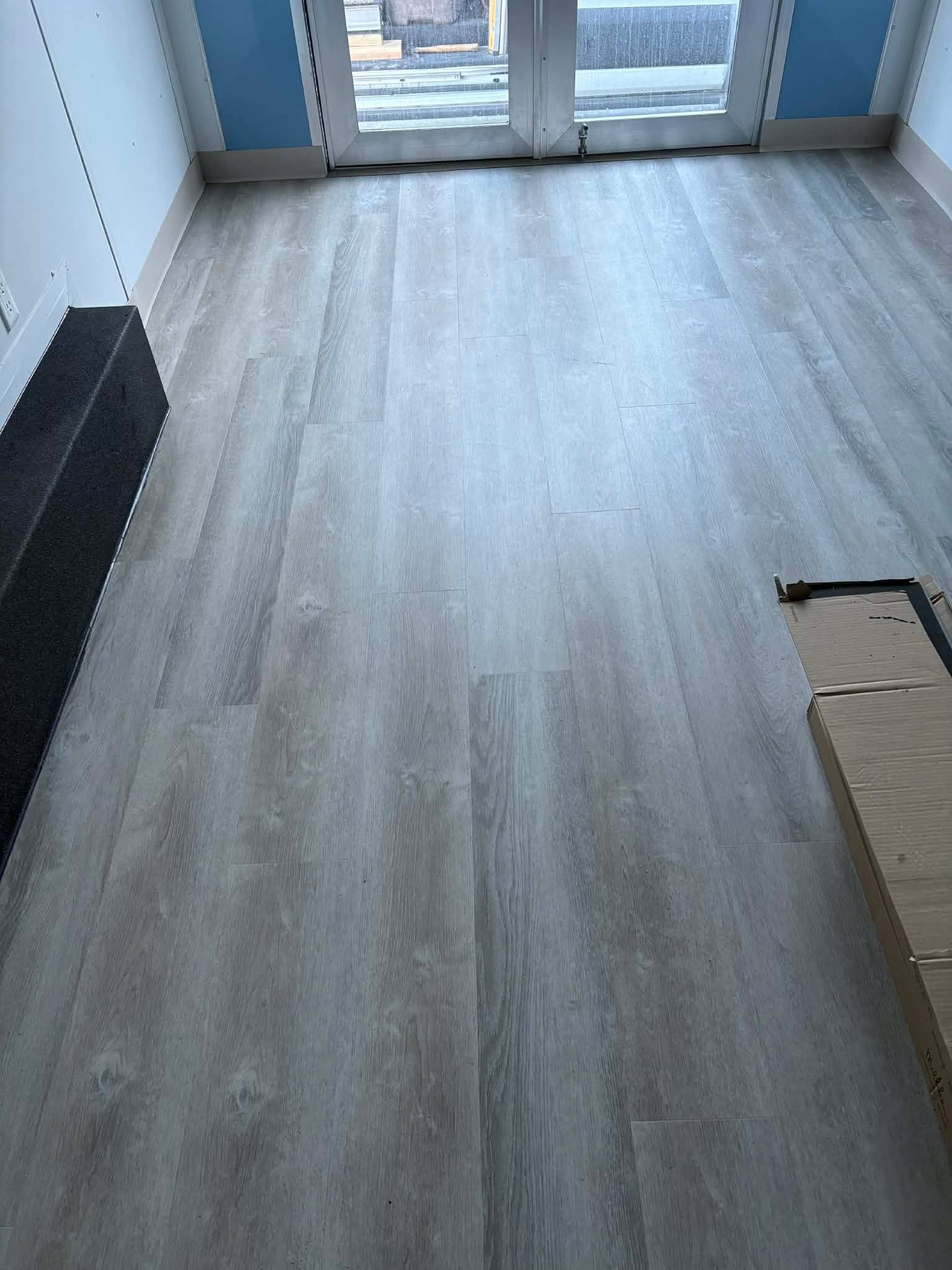 Light gray vinyl plank flooring installed in an entryway with glass doors and white walls.