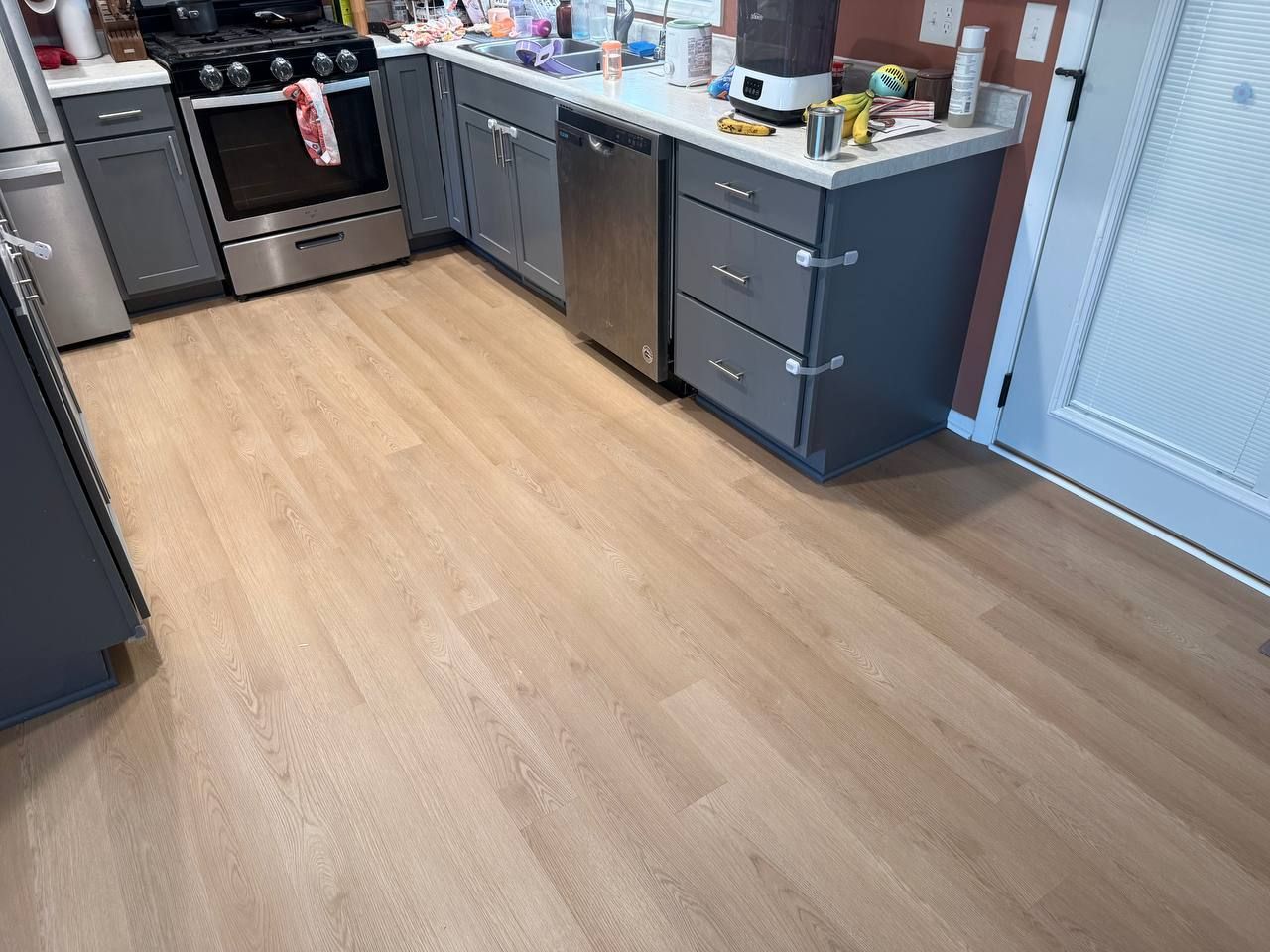 Light wood-tone LVP flooring installed in a kitchen with dark cabinets and stainless steel appliances.